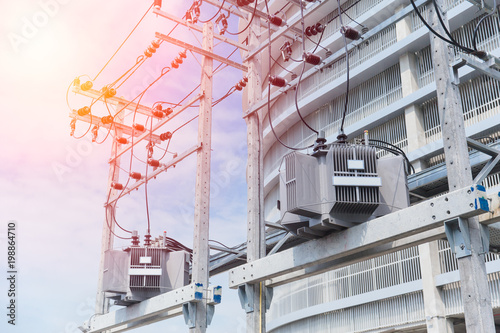 Power in urban: electrical post with power line cables transformers against office building