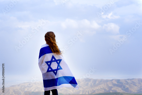 Canvas Print Little patriot jewish girl standing and  enjoying great view on the sky, valley and mountains with the flag of Israel wrapped around her