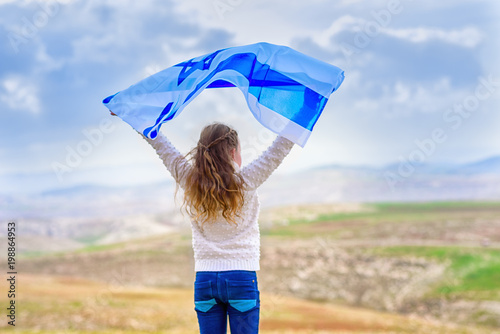 Little patriot jewish girl standing and enjoying with the flag of Israel on blue sky background.Memorial day-Yom Hazikaron, Patriotic holiday Independence day Israel - Yom Ha'atzmaut concept