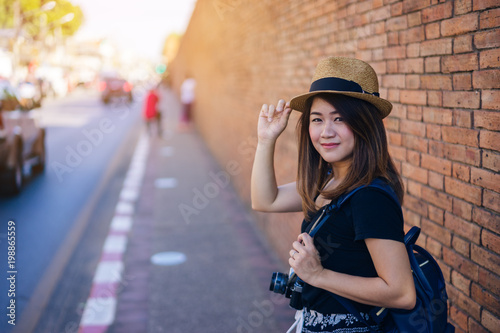 Tableau sur toile Young asian woman traveler with hat and bag using film camera traveling into  Tha Pae Gate at the old Chiangmai city in Chang Mai, Thailand