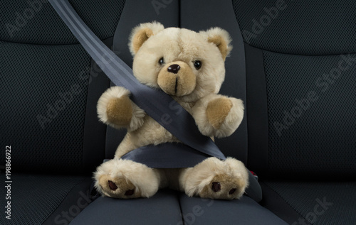 Teddy bear is sitting in a car fastened with a seat belt, represents child safety in a car