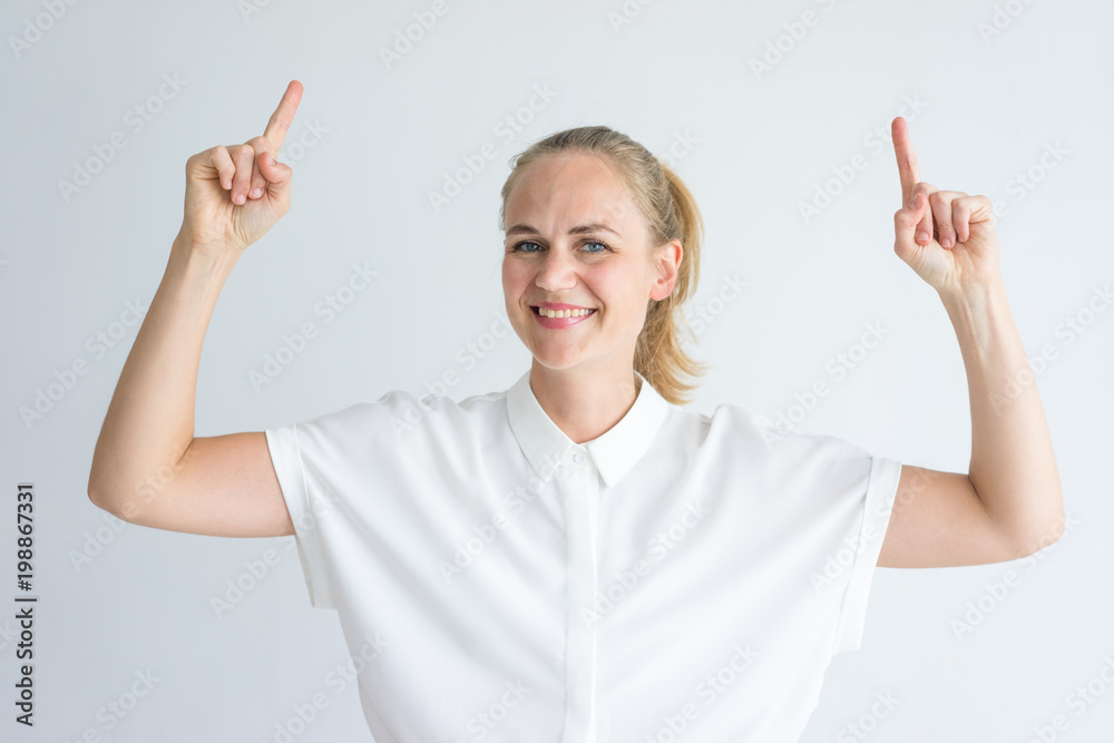 Portrait of cheerful young Caucasian woman wearing white shirt pointing upwards. Advertising concept Portrait of cheerful young Caucasian woman wearing white shirt pointing upwards. Advertising concept