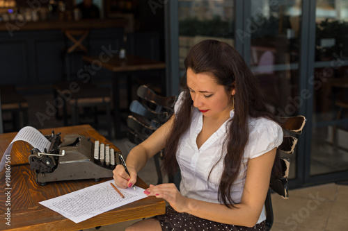 female writer with vintage typewriter making notes in a coffee s