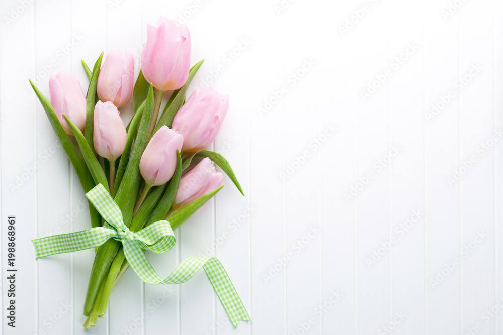 Obraz premium Fresh pink tulip flowers bouquet on shelf in front of wooden wall.