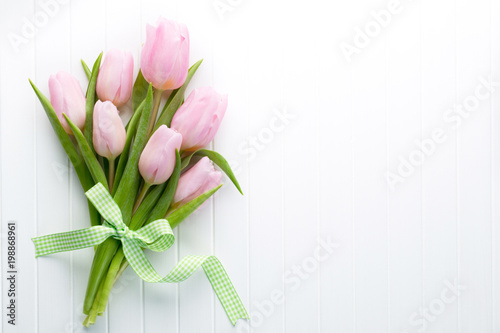 Fresh pink tulip flowers bouquet on shelf in front of wooden wall.
