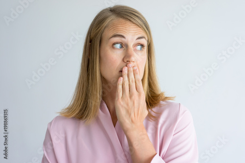 Portrait of shocked young Caucasian woman wearing pink blouse covering mouth with hand. Fear, bad breath concept photo