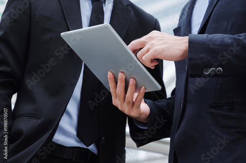 midsection two business asian smart man talking and reading information about finance news in mobile tablet together standing in modern city, network technology, internet, successful, teamwork concept