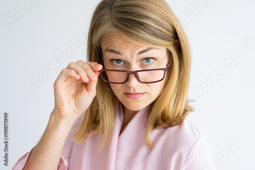 Frowning puzzled teacher looking surprised. Shocked displeased lady looking at camera over her glasses. Serious middle-aged woman wrinkling forehead and adjusting eyewear. Strictness concept