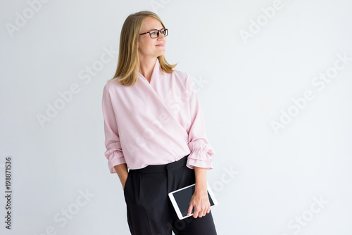 Pensive enterprising businesswoman thinking of new project. Smiling introspective confident female business executive holding tablet and looking away. Aspirations concept