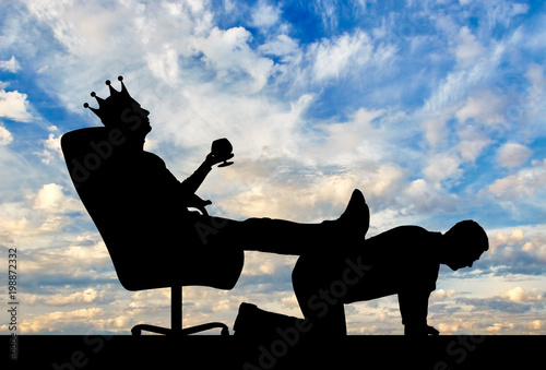 Silhouette of a selfish man with a crown on his head sitting in an armchair, threw back his legs on the man's back photo