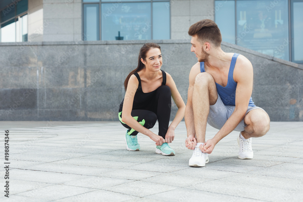 Happy man and woman tying shoelaces before running