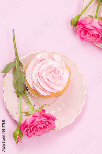 Cupcake with pink cream decoration and roses on pink pastel background.