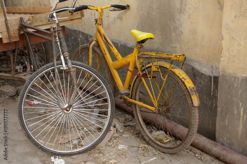 Rusty Yellow bike and a tricycle van in-front a wall. Old memories of Cycling. © Mashkawat Ahsan