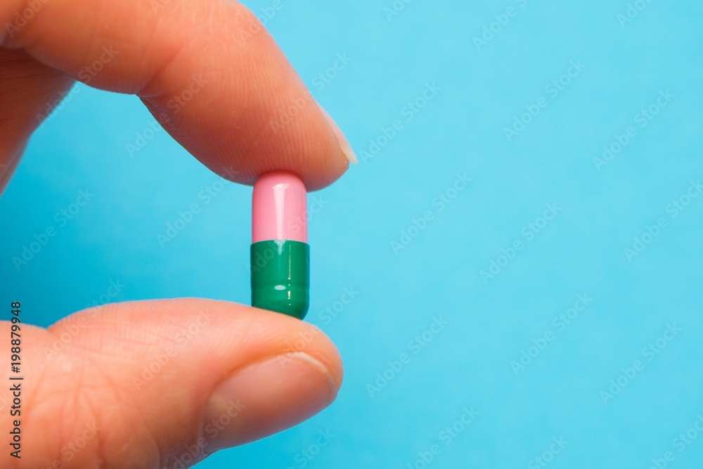 female hand holding a colored capsule on light blue background female hand holding a colored capsule on light blue background