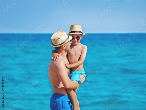 Father is holding his son in his hands whilen walking on a beach.