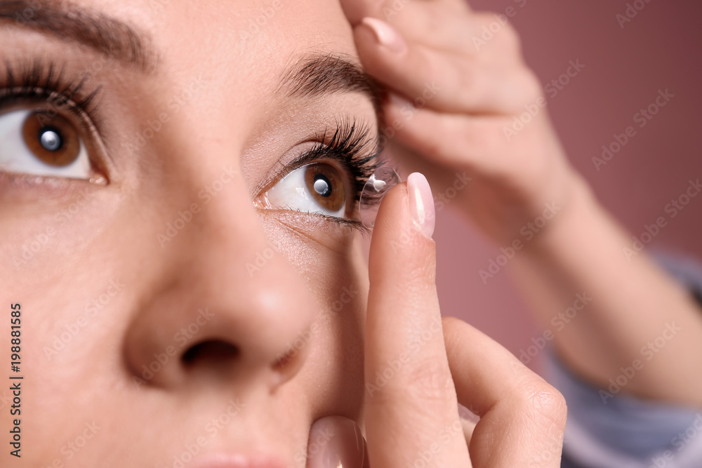 Young woman putting contact lens in her eye on color background Young woman putting contact lens in her eye on color background