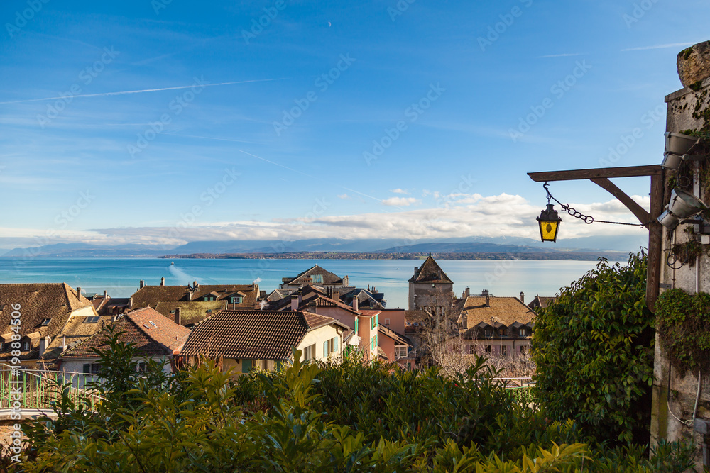 Beautiful view of the roofs in the old city Nyon and blue Leman lake. Blue sky and clouds. Switzerland