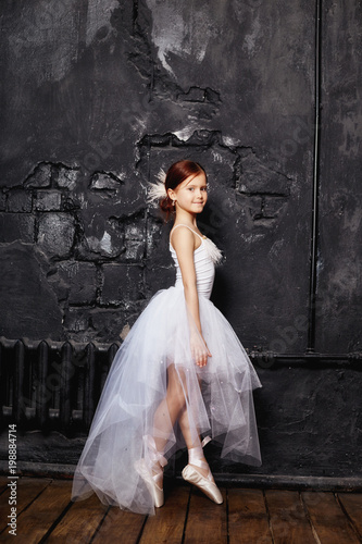 Girl in a white ball gown and shoes, beautiful red hair. Young theater actress. Little prima ballet. Young ballerina girl is preparing for a ballet performance