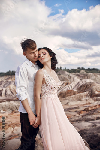 Couple in love in fabulous mountains hugging  Martian landscape. Lovers walk in the mountains in the summer  the girl in long light summer dress with a bouquet of flowers and a wreath on her head