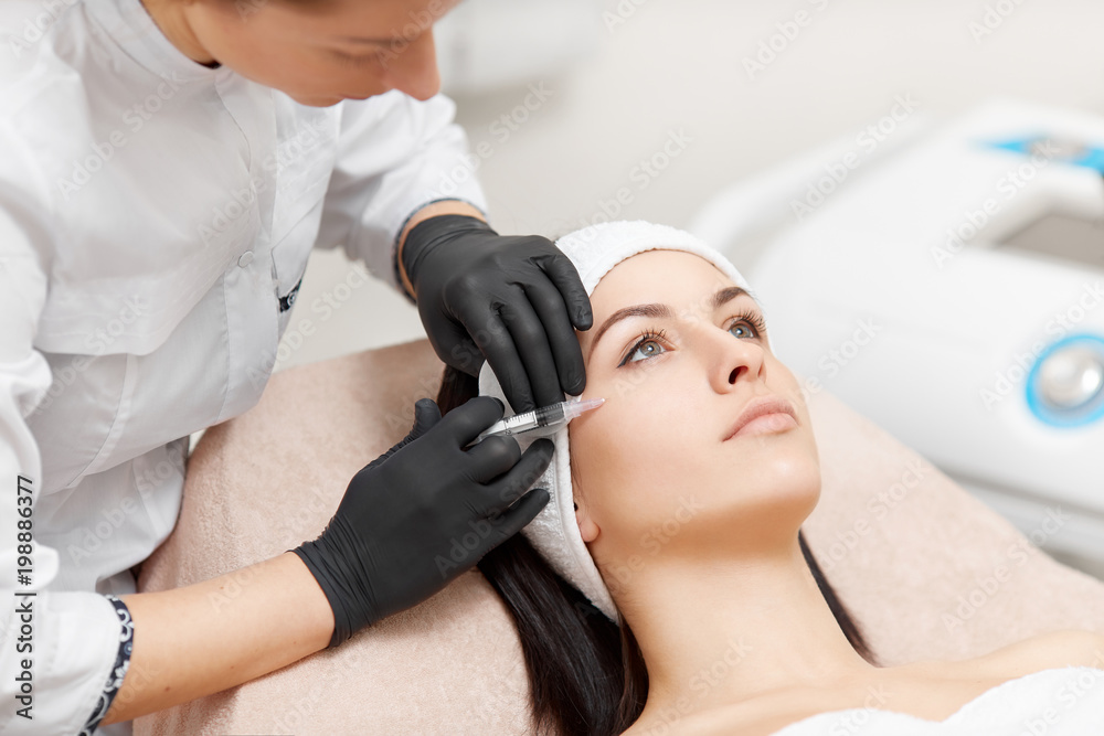 Beautician making anti-wrinkle injection in woman's face.