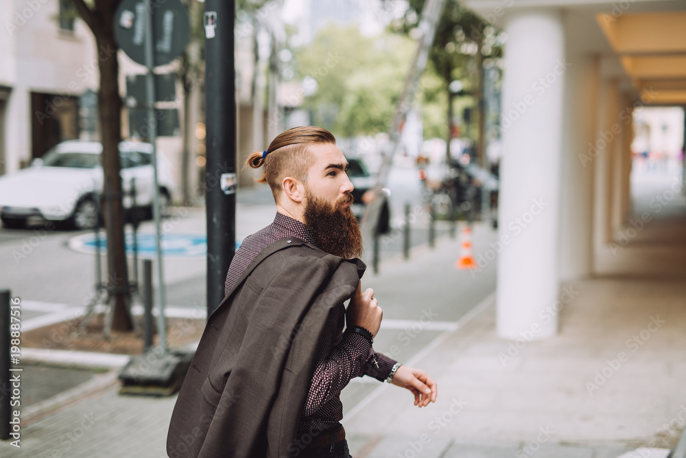Young man with the beard goes on the street. on the back you stylish classic jacket Young man with the beard goes on the street. on the back you stylish classic jacket