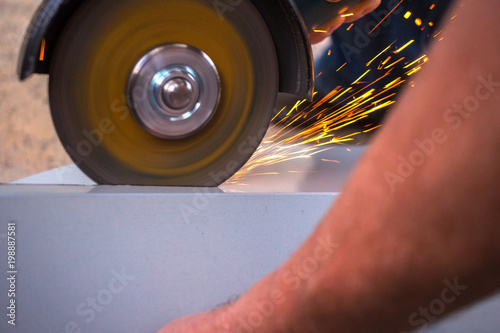 builder cuts a metal structure with spindles by a grinding machine.