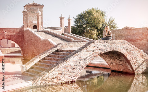 young female tourist in italy sitting on treponti bridge in comacchio medieval town