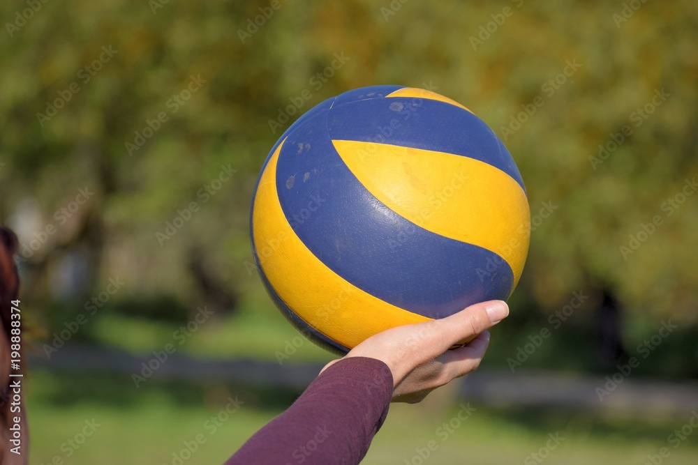 Image shows a hand holding a volleyball outdoors.