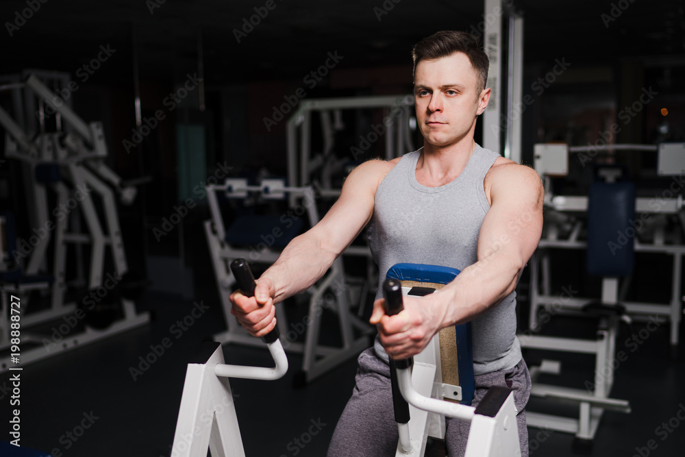 Fototapeta premium Strong handsome fit man exercising in the gym. Personal trainer workout. Athletic man working out his arms and chest muscles. Fitness, healhty lifestyle, bodybuilding concept.