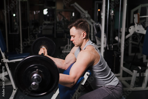 Strong handsome fit man exercising in the gym. Personal trainer workout. Athletic man working out his arms muscles with barbell on a bench. Fitness, healhty lifestyle, bodybuilding concept.