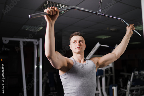 Strong handsome fit man exercising in the gym. Personal trainer workout. Athletic man working out his arms and chest muscles at upper block. Fitness, healhty lifestyle, bodybuilding concept.