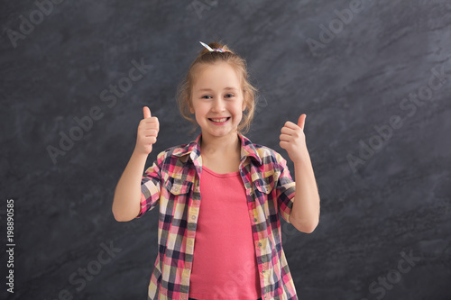 Casual little girl showing thumbs up at gray background