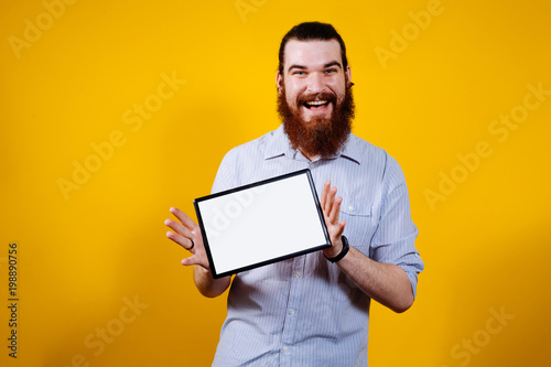 Cheerful man with beard holding tablet with empty blank white screen photo