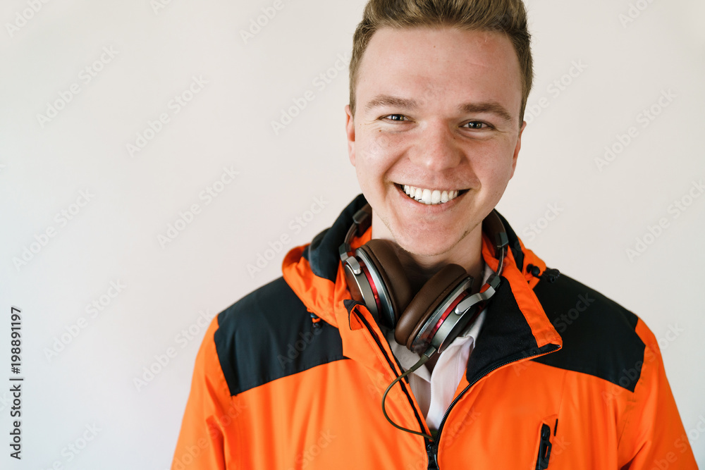portrait of a smiling young man in an orange jacket and headphones on a light background. Good mood and modern man. portrait of a smiling young man in an orange jacket and headphones on a light background. Good mood and modern man.