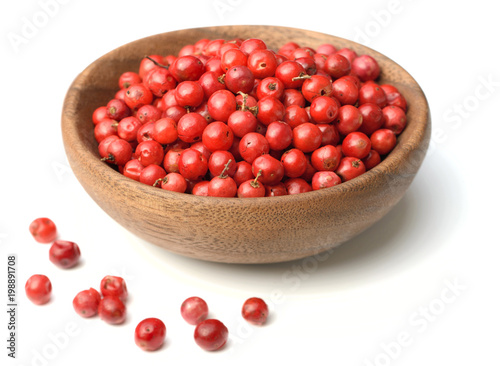 dried pink peppercorns in the wooden plate, isolated on white