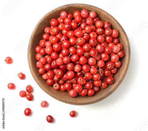 dried pink peppercorns in the wooden plate, isolated on white, top view