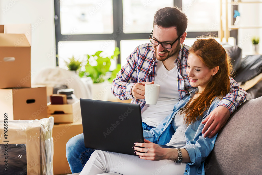 Young couple moving in new home. Sitting and relaxing after unpacking. Searching home decorating ideas on laptop Young couple moving in new home. Sitting and relaxing after unpacking. Searching home decorating ideas on laptop