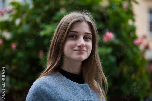 portrait of young smiling russian woman in dress near roses in a garden