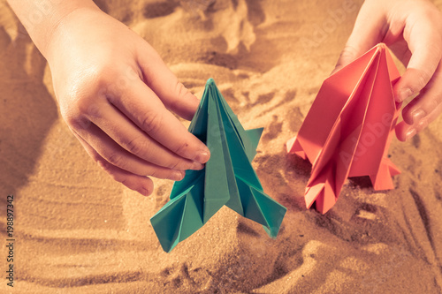Happy child boy playing with handmade origami paper, rocket on beach sand, start up concept