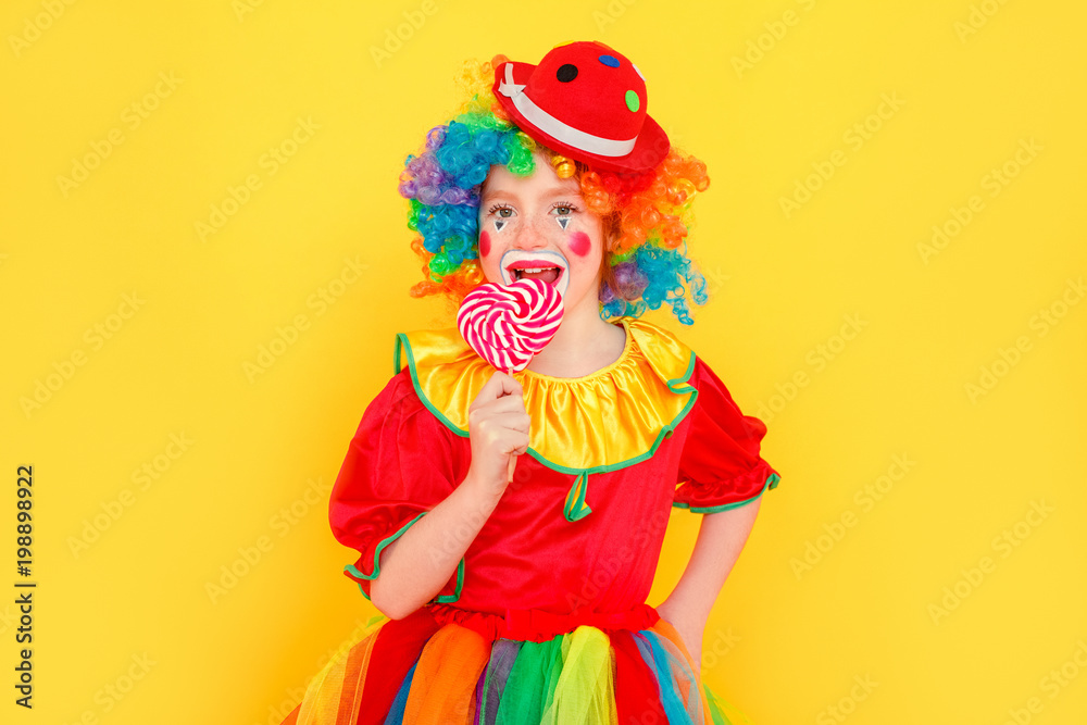 Cute little girl licks lollipop wearing clown costume toothy smiling Cute little girl licks lollipop wearing clown costume toothy smiling