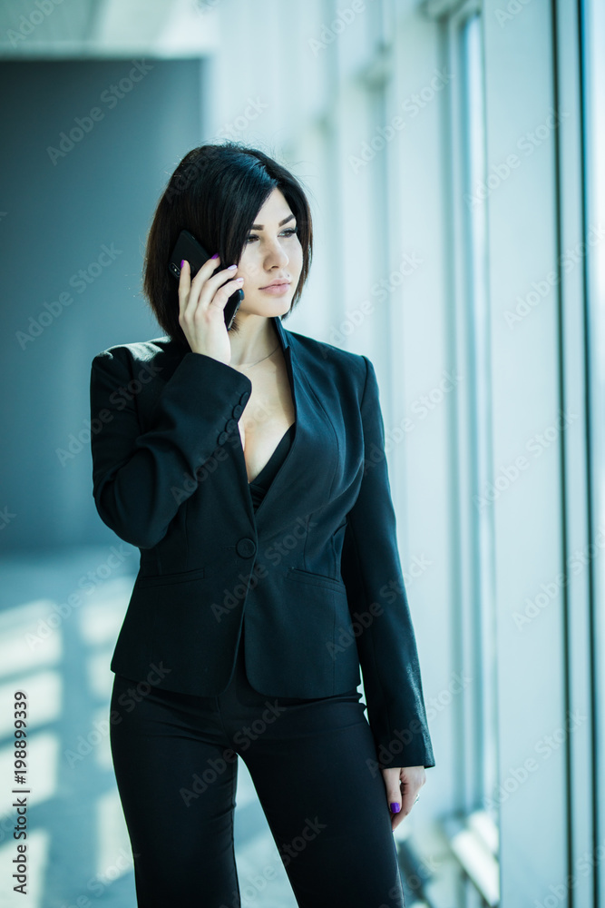 Businesswoman standing against office window talking on mobile phone in bright office