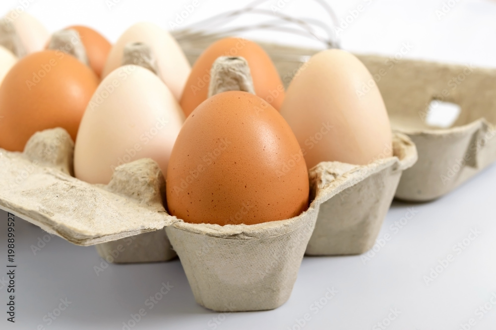 Fresh raw chicken eggs in carton box, on white background. Close-up  on brown and white eggs. The main ingredient for many dishes.
