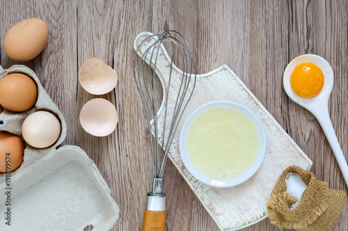 Fresh farm eggs on a wooden rustic background. Separated egg white and yolks, broken egg shells. Whipping eggs with whisk. Preparation of food from chicken eggs. The top view. View from above.