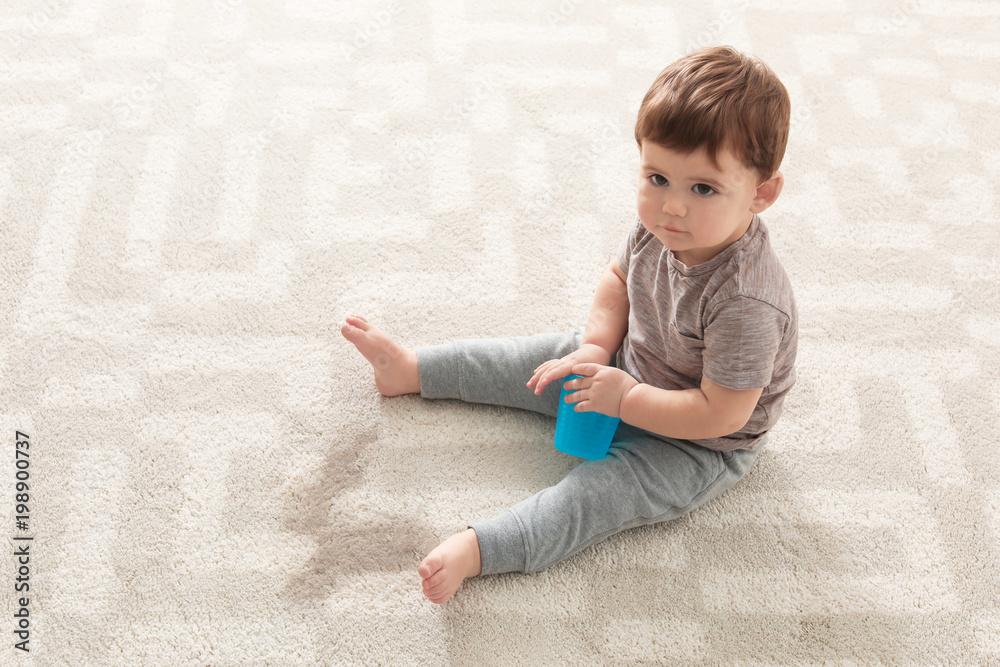 Naklejka premium Baby sitting on carpet with empty glass