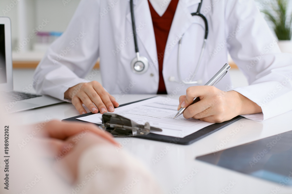 Close up of a female doctor filling up  an application form while consulting patient