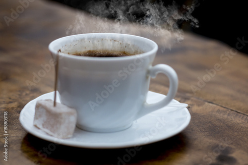 Steaming cup of Turkish coffee served with locum with tootpick in it, wood table, dark background and great contrast