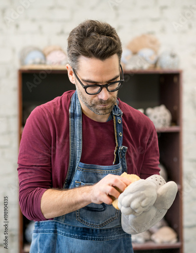 Portrait of Ceramist Dressed in an Apron Working on Clay Sculpture in Bright Ceramic Workshop. photo