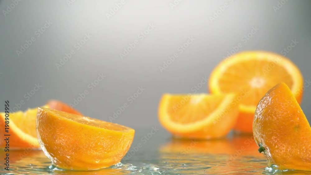 Orange hits orange juice surface and splits into halves. Slow motion shot