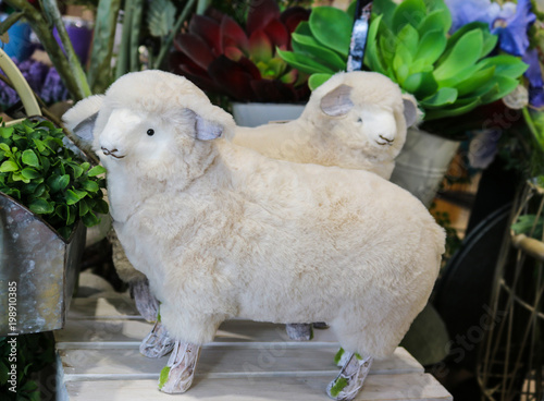 Two adorable decorative fabric and fur spring lambs in front of plants - selective focus photo