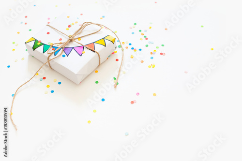 White gift box. Drawing of a colored garland, flags. White background. Confetti.